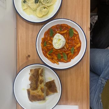 Tortelli - Three plates of Italian dishes—gnocchi with tomato sauce, a pastry, and pasta—are arranged on a wooden table. - Italian Near Me - Brooklyn, New York