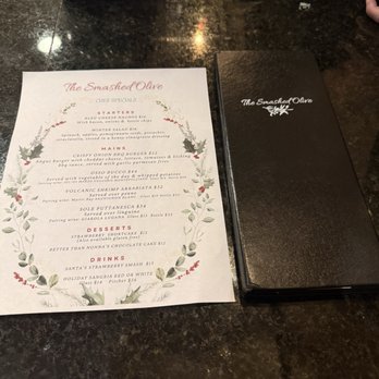 The Smashed Olive - A printed menu from The Smashed Olive restaurant is placed on a dark, polished countertop, alongside a black menu cover, keys, and a phone. - Soup Near Me - Washington, New Jersey