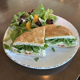 Pesto & Sundried Tomato Chicken Sandwich - A sandwich with arugula and vegetables, cut in half, is served on a white plate alongside a mixed green salad with orange segments.