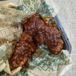 Sweet BBQ Blaze - Two glazed fried chicken pieces are placed on a black tray, wrapped in paper with green text, likely from a fast-food restaurant.