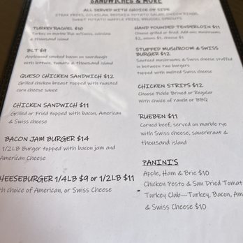 Cafe Grace - Lunch menu - A menu page from a restaurant offers a selection of sandwiches, burgers, and additional items. It includes dishes such as turkey Rachel, BLT, queso chicken sandwich, chicken sandwich, bacon jam burger, and cheeseburger. The menu also features hand-pounded tenderloin, stuffed mushroom Swiss burger, chicken strips, Ruben, and various paninis like apple, ham, and brie, chicken pesto, and turkey club. Prices range from $10 to $14, with descriptions of ingredients and preparation styles. - Breakfast & Brunch Near Me - Princeton, Illinois