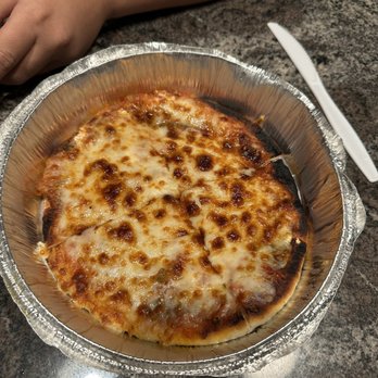 Cedar Tree - Pizza - A cheese pizza with melted cheese and browned spots in a foil container on a granite table, with a plastic knife nearby. - Mediterranean Near Me - River Vale, New Jersey