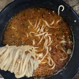 30. Dan Dan Noodles - A bowl of spicy ramen with bean sprouts, green onions, and noodles in a broth, served in a black bowl on a wooden table.