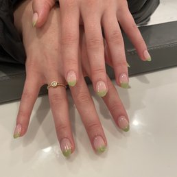 dip with arylic with french tip!! - Close-up of hands with manicured nails painted with green tips, resting on a white surface, with a gold ring on one finger.