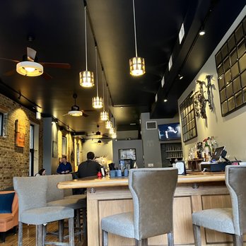 J9 Wine Bar - the bar and seating - A wine bar interior featuring a wooden bar counter, upholstered chairs, exposed brick walls, and artwork, with pendant lighting and ceiling fans. - Wine Bars Near Me - Chicago, Illinois