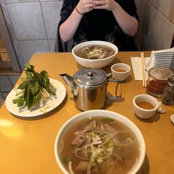 Saigon Boy Noodle House - Table with two orders of noodle soup #8 with beef. Bean sprouts and basil, green tea, and cutlery also on table.