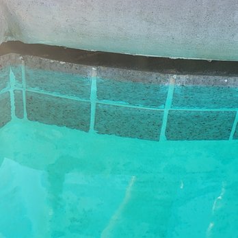 Paul's Pool Magic - The image shows the edge of a swimming pool with a tiled border made of rectangular tiles in shades of gray and black. The water in the pool is clear and reflects the tiles and surrounding area. The photo captures the transition from the pool's interior to the tiled edge, emphasizing the clean and maintained condition of the pool. - Pool Cleaners Near Me - Riverside, California