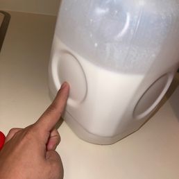 a hand pointing at a container of milk - A hand presses a circular button on a large, white plastic container with a textured top surface.