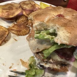 Half eaten Bacon Mushroom Swiss Burger with chips.