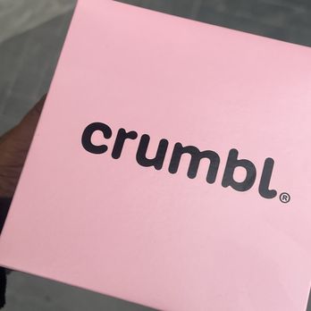 Crumbl - Wayne - A pink Crumbl cookie box is held by a person, with a gray tiled floor in the background. - Bakeries Near Me - Wayne, New Jersey