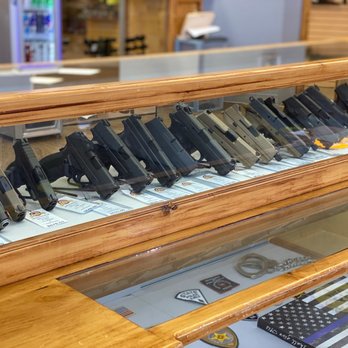Calibers - Handguns and support the blue! - A glass display case showcases multiple handguns and firearm accessories in a gun shop, with tags and labels visible beneath each firearm. - Firearm Training Near Me - Clovis, New Mexico