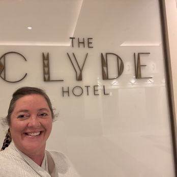 The Clyde Hotel - A woman with a smile is holding a camera or phone to take a selfie in front of a sign that displays 'The Clyde Hotel.' The sign is mounted on a light-colored wall, and the woman appears to be inside the hotel lobby or entrance area. The photo captures her face and part of her upper body, with the hotel sign clearly visible behind her. - Hotels Near Me - Albuquerque, New Mexico