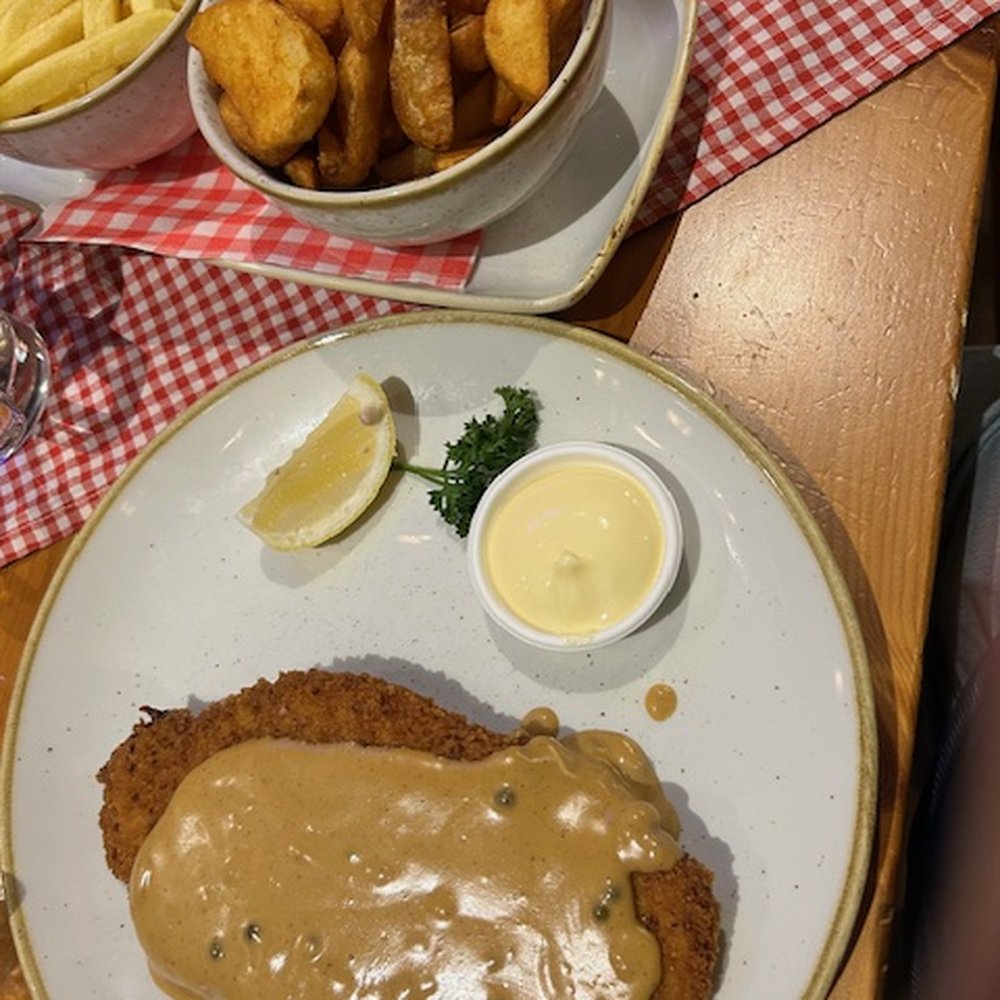 Schnitzelparadies - Traditional schnitzel (200g) with pepper sauce.  Potato wedges and french fries in the background. - German Near Me - Roermond, LI