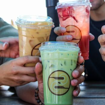 Ziggi's Coffee - Friends holding up three iced Ziggi's drinks--iced latte, green matcha drink, and red strawberry refresher. - Coffee & Tea Near Me - Bentonville, Arkansas