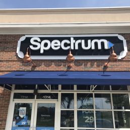 Spectrum's storefront displays a sign with the company name, a blue awning, and glass doors with promotional posters.