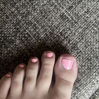 Oasis Nails & Spa - A close-up of a foot with pink-painted toenails, some of which are chipped, on a woven textured surface. - Nail Salons Near Me - Bloomington, Illinois