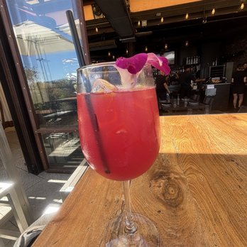Rooftop - Pear on me - A pink-colored cocktail with ice and an orchid flower garnish is placed on a wooden table at a restaurant with an open-air setting. - New American Near Me - Walnut Creek, California