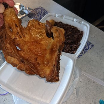 El Cubano - Fried chicken - A hand holds a piece of fried chicken over a takeout container filled with rice and black beans, on a kitchen counter. - Cuban Near Me - Lancaster, Pennsylvania