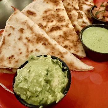 Ayayay - Quesadilla made with chicken - A quesadilla made with chicken is served with guacamole and green sauce in small black cups, on a red plate. - Mexican Near Me - Chicago, Illinois