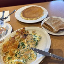 Pancakes - A breakfast plate with scrambled eggs, hash browns, and a knife, along with a stack of toast, a pancake, and condiments on the table.