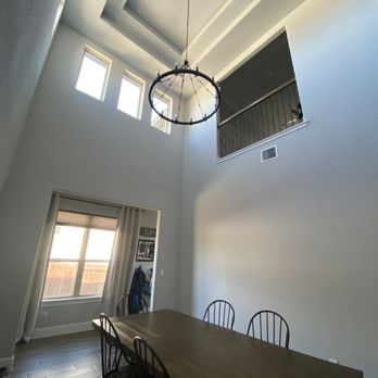 EJ Tech - New and improved chandelier...looks so majestic! - A dining area features a wooden table with six chairs, a large window with curtains, and a high ceiling with a circular chandelier. - Electricians Near Me