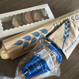 Cookies - A selection of baked items from Breadsmith, including a baguette, a cookie assortment, and an almond croissant, on a wooden table.