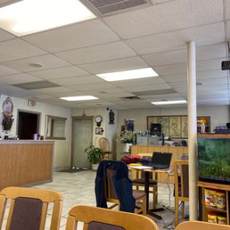 a restaurant with a fish tank in the middle of the room - A room with wooden chairs and tables, a reception counter, and various decorations on the walls, including a clock and artwork.