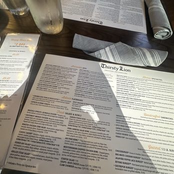 Thirsty Lion - A table setting at Thirsty Lion includes menus, cloth napkins, a glass of water, and a water pitcher, with a person visible in the background. - American Near Me - Euless, Texas