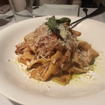 Ristorante Euno - Pappardelle Panna e Prosciutto - A plate of pasta with a generous topping of grated cheese, fresh basil leaves, and sauce, served on a white dish. The setting includes a table with glasses and utensils, indicating a restaurant environment. - Italian Near Me - Boston, Massachusetts
