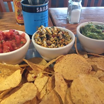 Hooks Chill & Grille - Yummy - Three bowls of salsa, corn salad, and guacamole are arranged on a tray with tortilla chips on a wooden table at a restaurant. - Mexican Near Me - Ogunquit, Maine