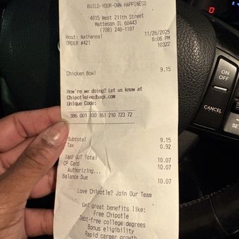 Chipotle Mexican Grill - A person is holding a Chipotle Mexican Grill receipt in their left hand inside a vehicle. The receipt displays the restaurant's logo, address, date, time, and order details including a chicken bowl costing $9.15. The background shows part of the vehicle's dashboard and steering wheel. The receipt includes promotional text about joining the Chipotle team and benefits. - Mexican Near Me - Matteson, Illinois