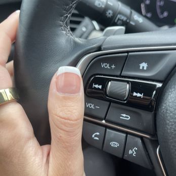 Legend Nails - Frankfort - Nails - A hand with a gold ring is gripping a car steering wheel, with the thumb near audio control buttons and a home button, inside a vehicle. - Nail Salons Near Me - Frankfort, Illinois