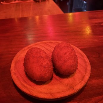 Bar Isabel - Croqueta - Two croquetas are placed on a round wooden plate on a bar counter at Bar Isabel in Toronto, with warm lighting and bar equipment in the background. - Spanish Near Me - Toronto, Ontario