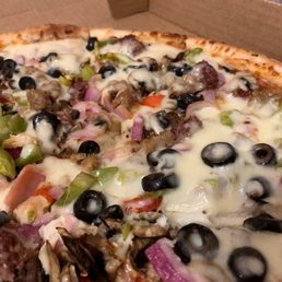 Cheese Pie - A pizza with a golden crust topped with melted cheese, black olives, green peppers, red onions, and sausage slices, served in a cardboard pizza box. The toppings are spread evenly across the pizza, with some cheese slightly browned.