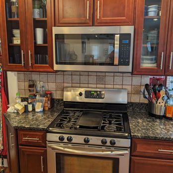 Best Yet Installations - New microwave installed between wood-panel shelves - A kitchen featuring wooden cabinets, a stainless steel microwave above a gas stove, and a granite countertop with kitchen utensils and supplies. - Electricians Near Me - Spencer, Massachusetts