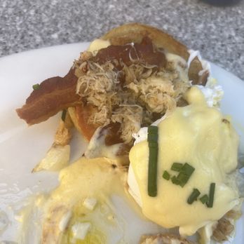 Egg N' Joe - Dungeness Crab Benedict lacking the amount of crab as expected. - Eggs Benedict topped with crab meat, bacon, and hollandaise sauce, served with chopped chives on a white plate. - American Near Me - Gilbert, Arizona