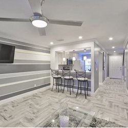 Floorit Enterprises - Living Room Renovation with stripped accent wall, herringbone tile floors, recess can lighting, white crown molding and baseboards.