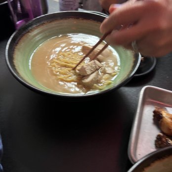 Doragon Eatery - Plain Ramen - A bowl of ramen with broth, noodles, and a piece of meat, with a person using chopsticks to pick up the meat. - Ramen Near Me - Ashland, Massachusetts