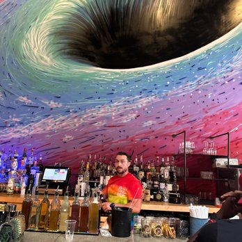 Roosevelt Bar - a man standing at a bar with a giant black hole in the background - Cocktail Bars Near Me - Beacon, New York