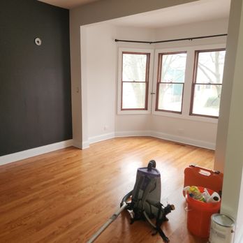 Rapid Response Restoration - A vacant living room features hardwood flooring, white walls, and a bay window with three sections. Cleaning equipment and supplies are visible in the foreground. - Damage Restoration Near Me - Chicago, Illinois