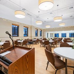 Bozeman Event Space - Spacious ballroom featuring a podium with mic, projector, and elegant banquet seating. Ideal for conferences, trainings, and celebrations.