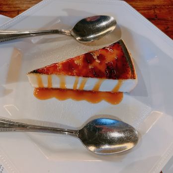 Kitchen and Rail - A slice of cheesecake with caramel sauce is served on a white plate, accompanied by two silver spoons, with a menu partially visible underneath. - Bars Near Me - Eagan, Minnesota