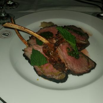 The Bygone - Lamb - Cooked lamb slices garnished with mint leaves are served on a white plate, with a small dollop of sauce or puree nearby. - American Near Me - Baltimore, Maryland