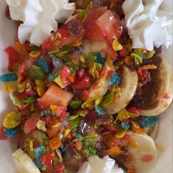 The Blend - 12 ct pancakes w/ strawberries, bananas, fruity pebbles, whipped cream, caramel, and original syrup - A dessert dish contains sliced bananas and strawberries topped with whipped cream and a generous layer of multicolored cereal pieces, served in a paper tray. The presentation includes fresh fruit, creamy whipped topping, and crunchy cereal, creating a mix of textures and flavors. - Juice Bars & Smoothies Near Me - Albuquerque, New Mexico