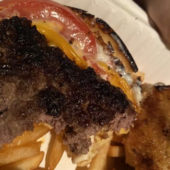 Beacon Barking Frog - That's an Indian Point style burger. I'm surprised I ate that much but everything was already closed - The image features a close-up of a burger with a visibly charred beef patty, topped with slices of tomato and melted cheese. French fries are visible in the foreground, and the burger is served on a white paper-lined surface. The focus is on the burger's ingredients and cooking style, with a casual dining presentation. - Sports Bars Near Me - Beacon, New York