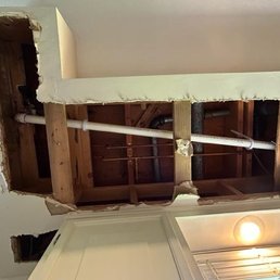 A wall has been cut open, revealing plumbing pipes, wooden studs, and insulation inside the wall cavity.