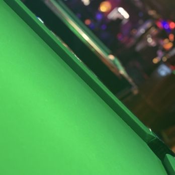Nu Towne Saloon - The image shows a close-up of a green pool table surface with a smooth, felt texture. The background is out of focus, displaying multicolored lights and shapes, suggesting an indoor environment such as a bar or game room. The focus is on the pool table, with the edge and part of the playing surface visible. - Gay Bars Near Me - Phoenix, Arizona