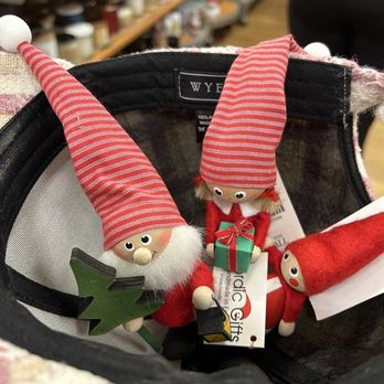 TJ Maxx - cute little santa & elves. - Three elf-themed Christmas ornaments with red and white striped hats are inside a store basket, with shelves of craft supplies visible in the background. - Men's Clothing Near Me - Clovis, California