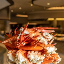 Crab Legs - A plate filled with cooked crab legs, stacked in a pile, with a blurred indoor setting in the background.