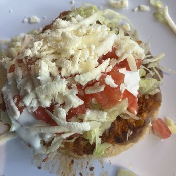 Taco City - This  Sope de Tinga makes me never need to eat a taco again. It's so good!! Happy this is in my neighborhood. - A close-up of a taco on a white plate, topped with shredded cheese, chopped lettuce, diced tomatoes, and sour cream. The taco shell appears crispy, and some ingredients are spilling onto the plate, indicating a freshly prepared dish with typical Mexican toppings. - Mexican Near Me - Chicago, Illinois